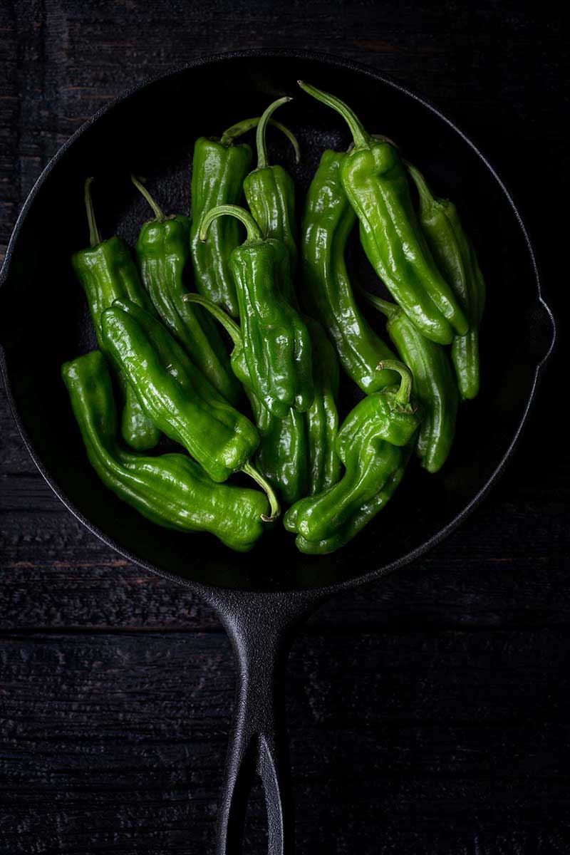 Fresh, uncooked green chili peppers in a cast iron skillet.