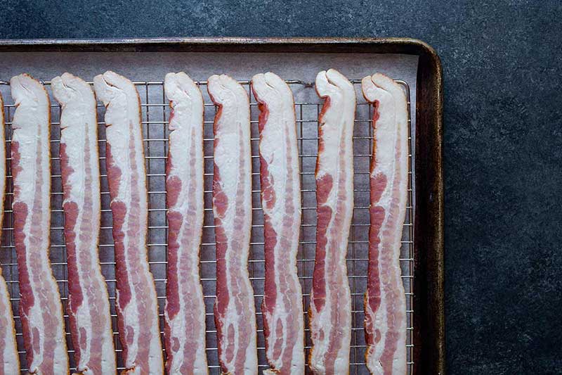 Raw bacon lined up on a sheet pan.