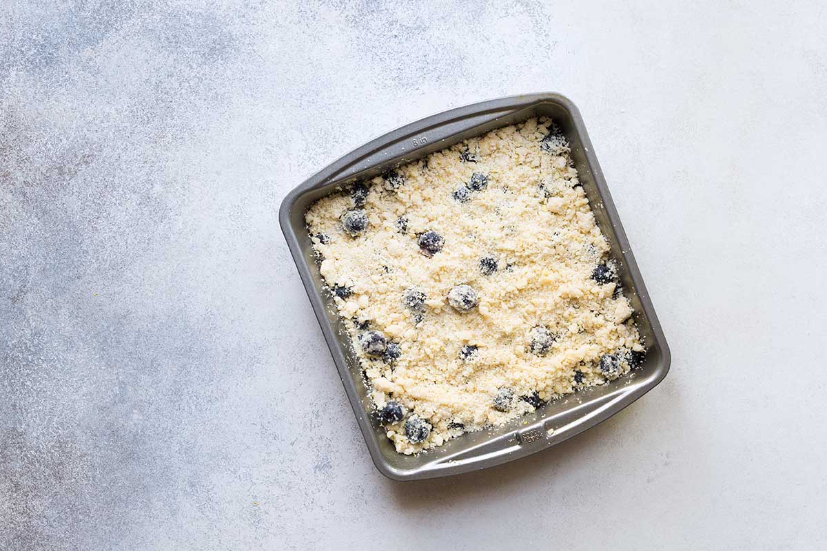 Blueberry crumble bar ingredients in an 8x8 inch pan.