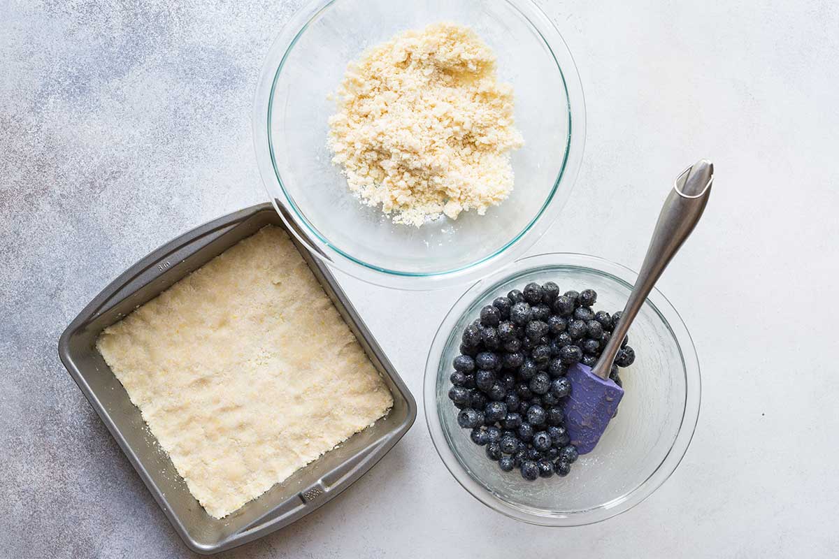 Ingredients to layer blueberry crumb bars, including blueberries and topping.