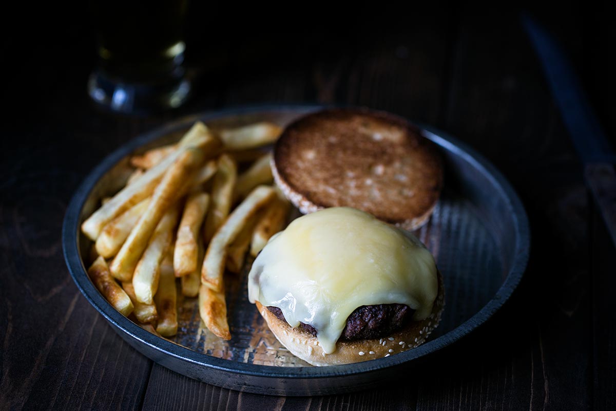 A closeup shot of hot raclette cheese on a grilled burger.