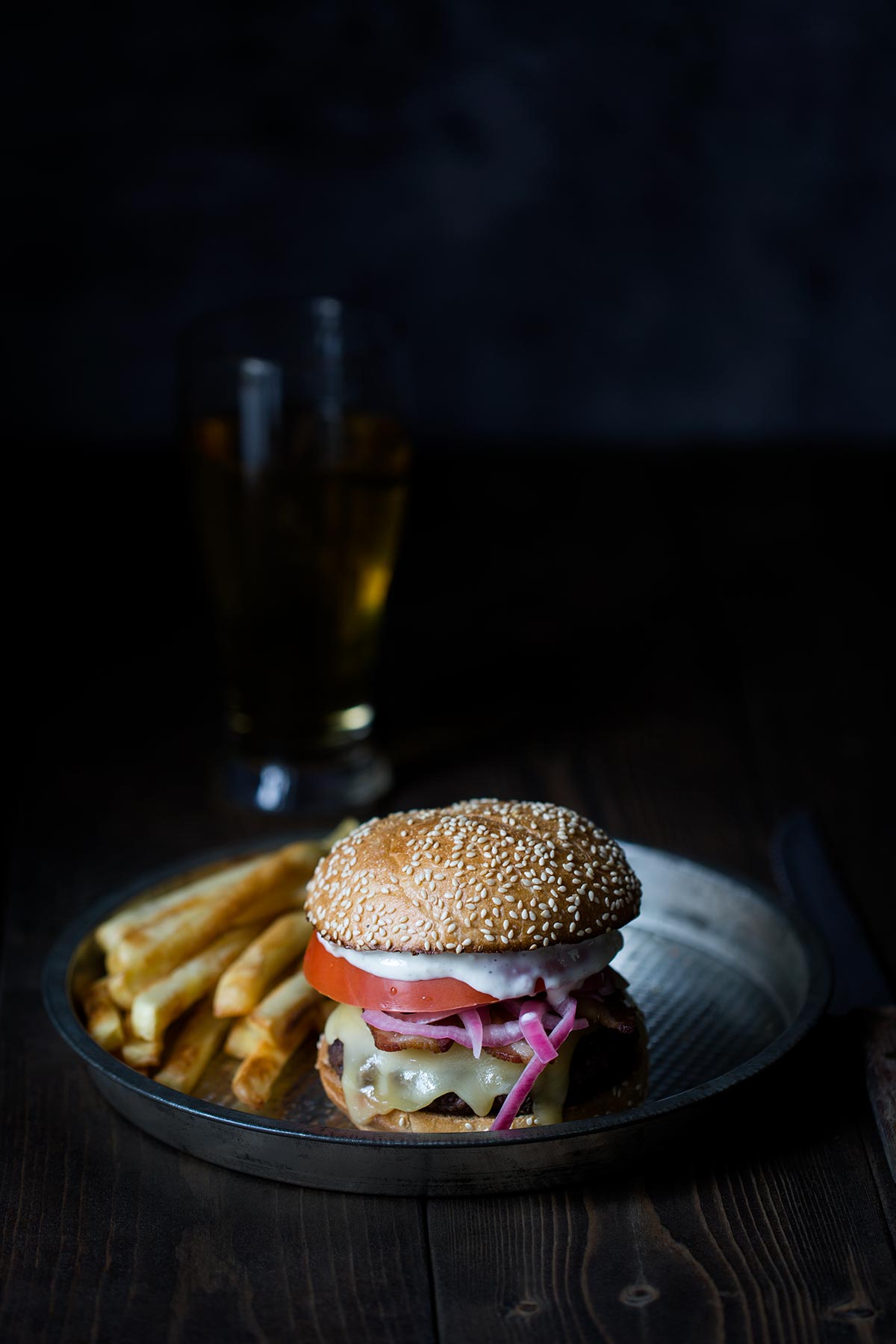 A burger topped with raclette cheese, pickled shallots, tomato, and aioli.