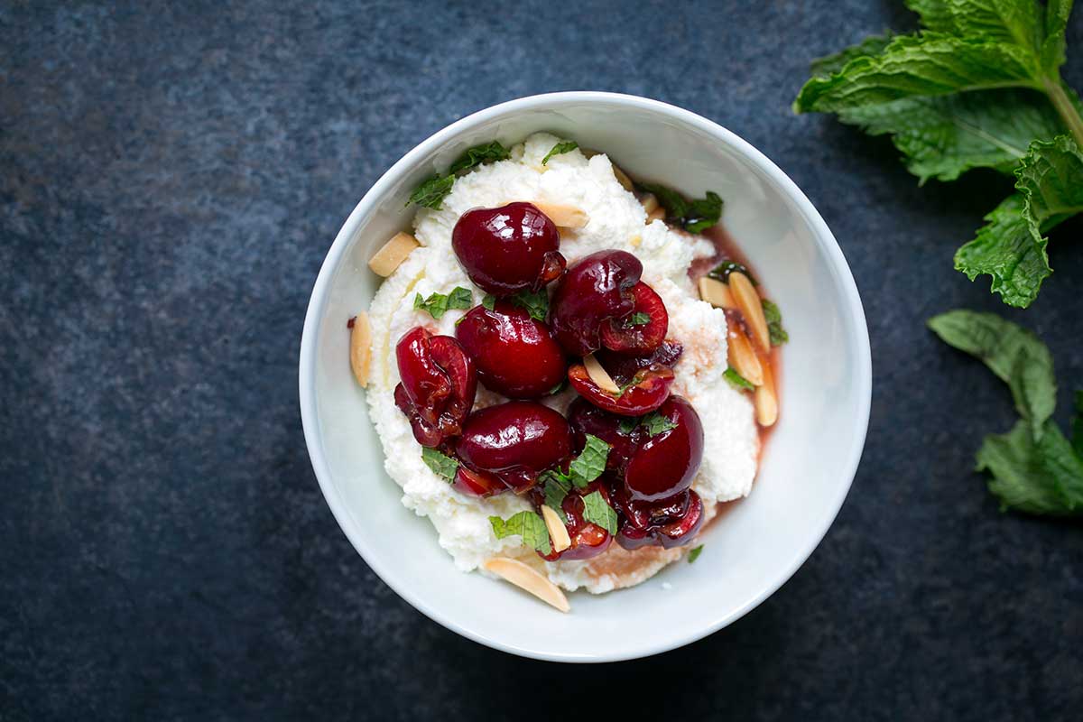 A macerated cherries recipe in a bowl with ricotta cheese, almonds and mint.
