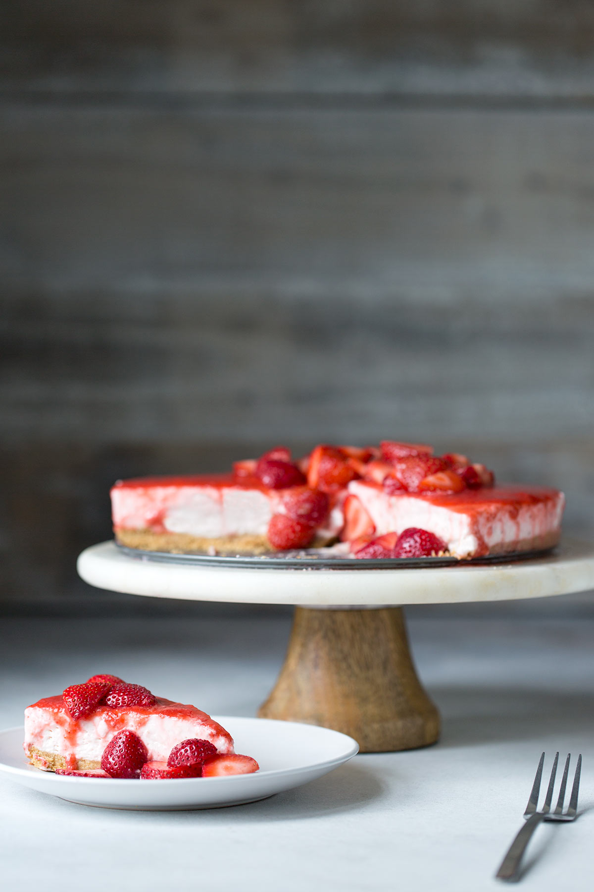 A slice of no-bake strawberry cheesecake in the foreground, the full cake in the background.