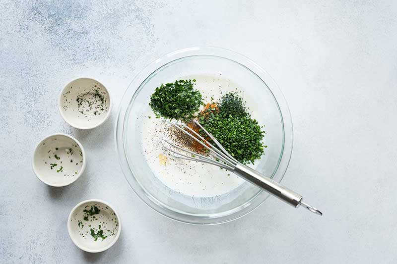 A mixing bowl filled with ingredients for buttermilk ranch dressing and a whisk. 