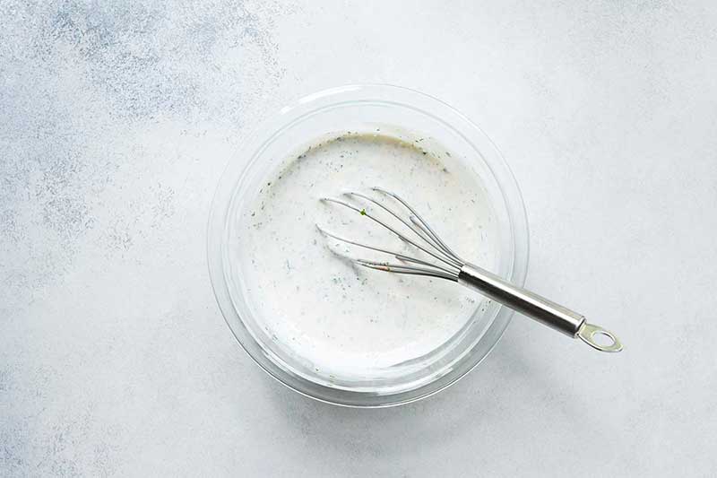 A mixing bowl filled with finished buttermilk ranch dressing and a whisk. 