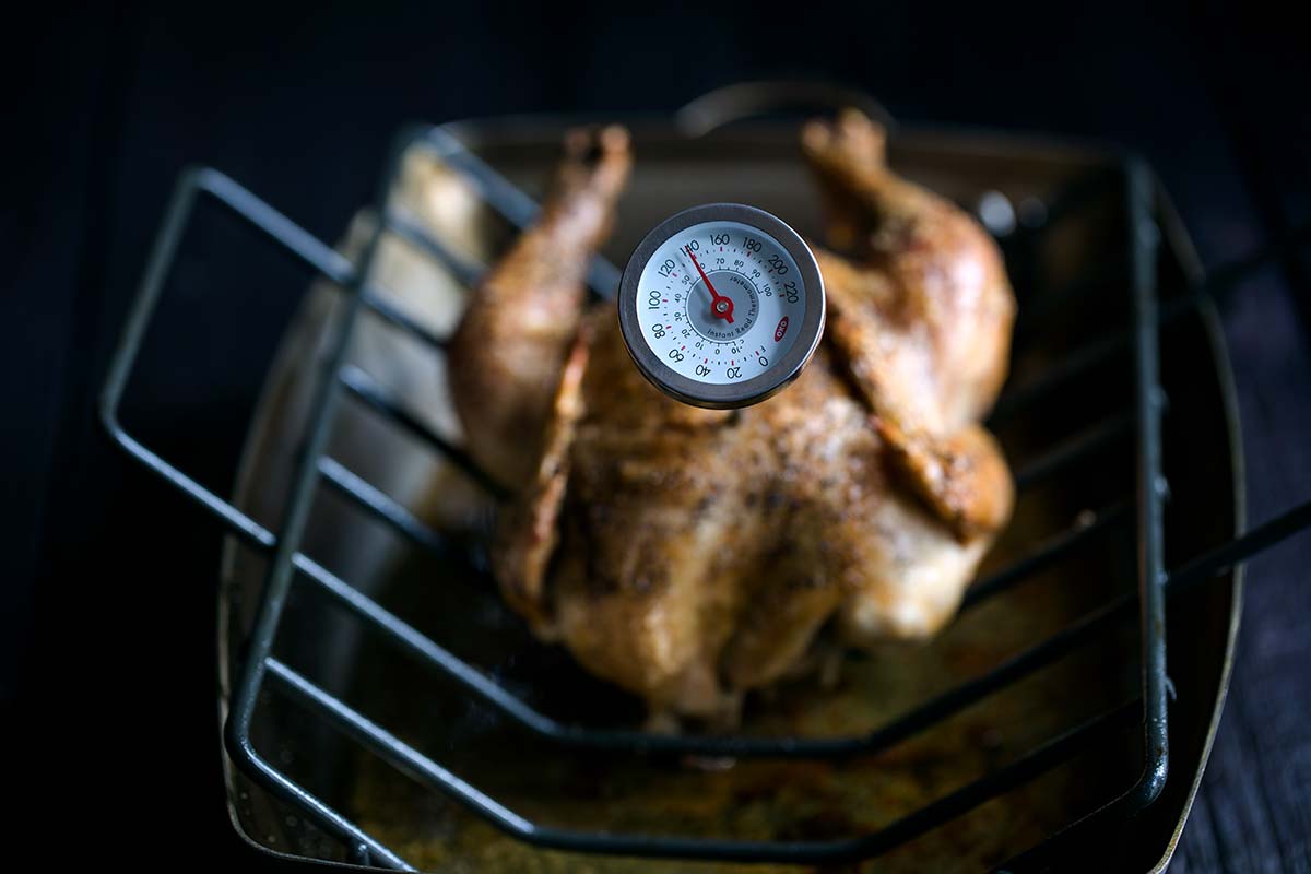 A roasting pan with a whole roasted chicken and a thermometer