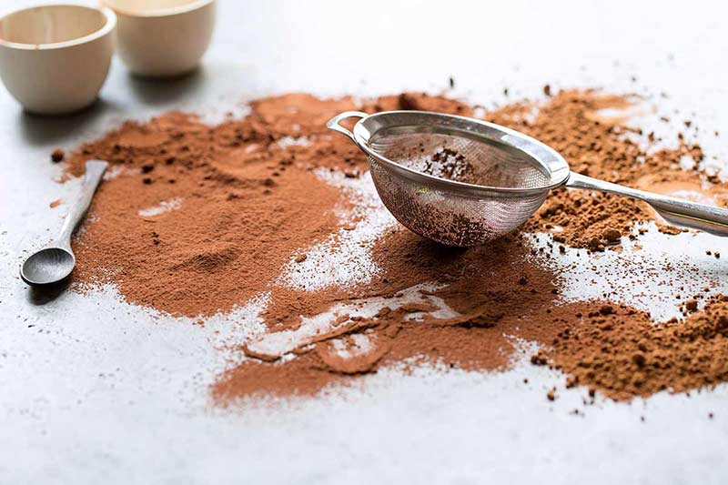 A small fine mesh strainer sitting over cocoa powder that has been sifted