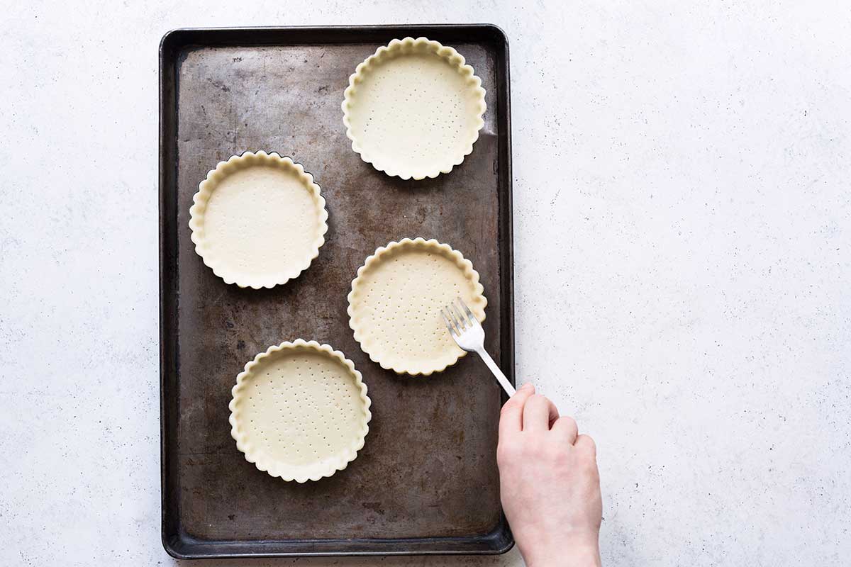 Using a fork to prick holes in the dough before blind baking the tart shell.