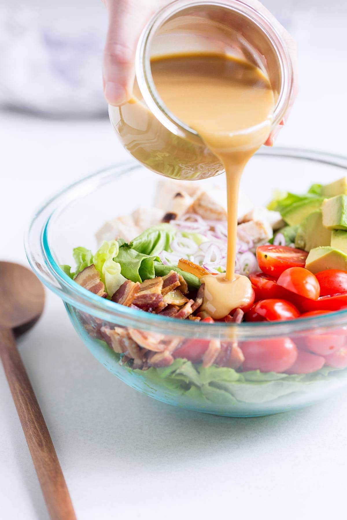 A side angle photo of honey mustard dressing being poured onto chicken bacon avocado salad