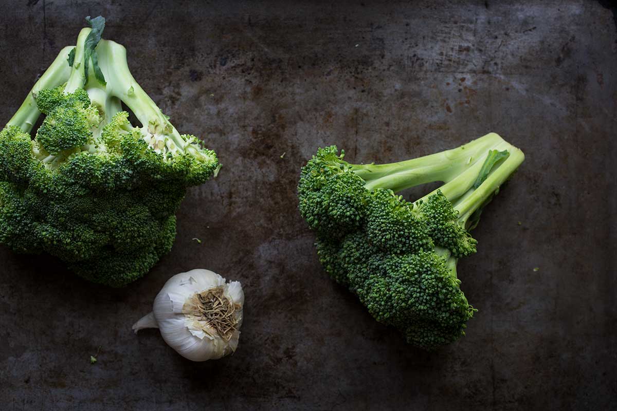 Raw broccoli and a whole head of garlic on a sheet pan