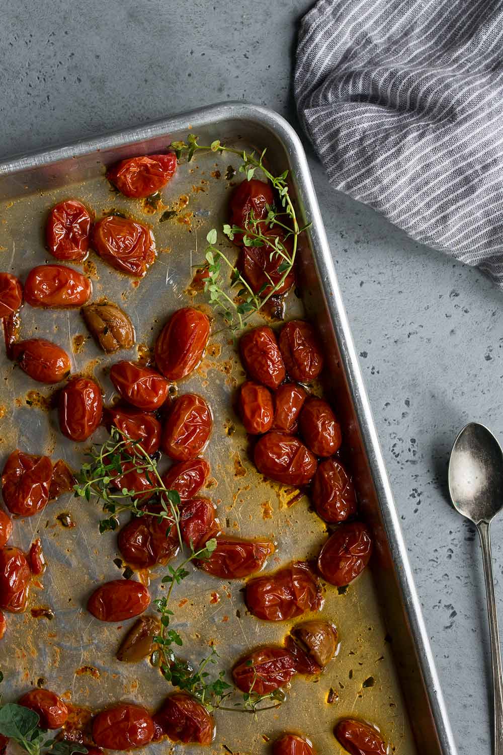 Oven roasted tomatoes on a sheet pan, fresh from the oven, topped with sprigs of thyme.