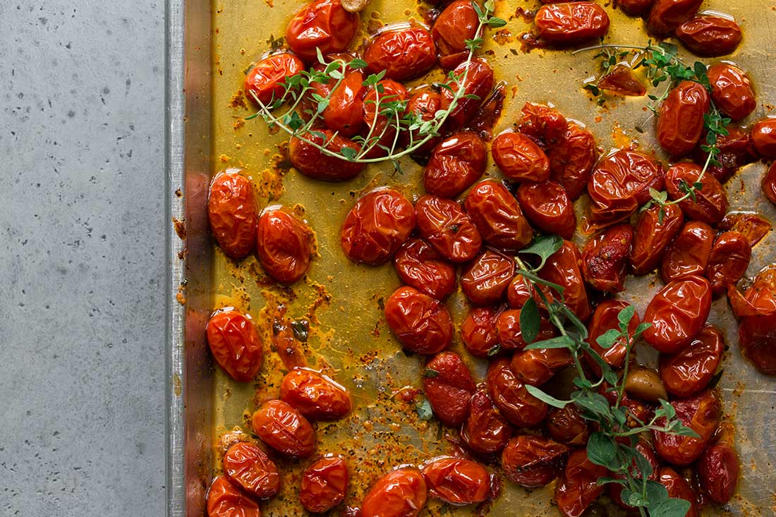 Roasted grape tomatoes, fresh herbs, and infused olive oil on a sheet pan.