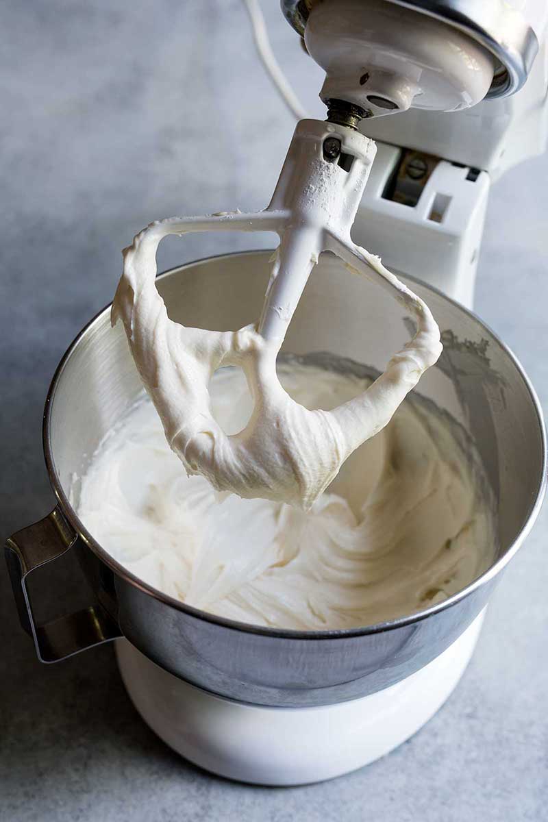 A stand mixer fitted with the paddle attachment lifted to show the finished cream cheese frosting recipe.