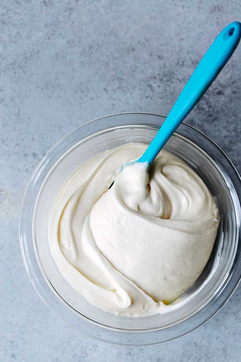Cream cheese frosting recipe in a bowl with a blue spatula