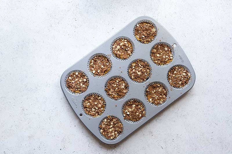 Pumpkin muffin batter in a muffin tin, topped with streusel, before baking.
