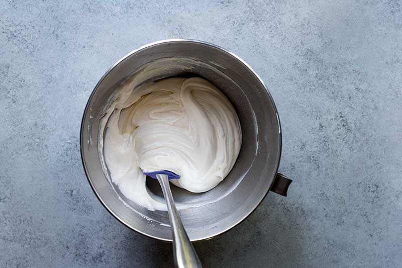 An overhead shot of homemade cream cheese frosting in a stand mixer with a spatula.