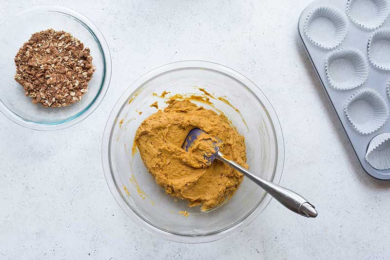 Ingredients for homemade pumpkin muffins recipe in a pyrex bowl, mixed with a spatula.