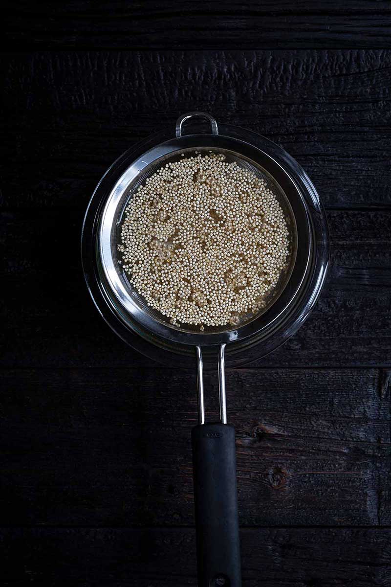white quinoa being soaked in cold water with a fine mesh strainer