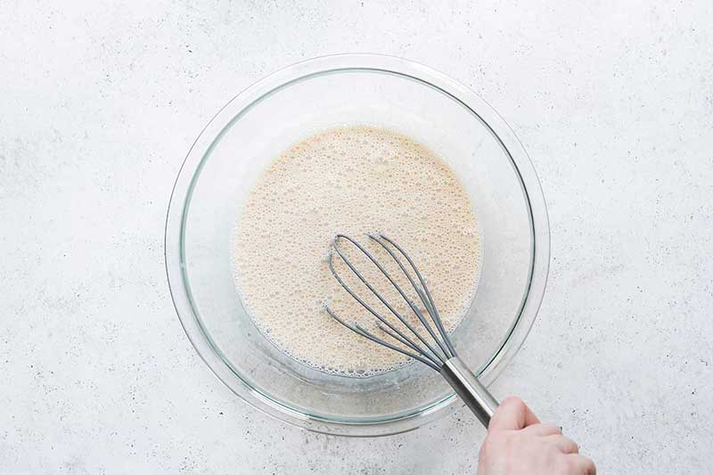 A bowl and whisk with ingredients for no-churn ice cream, including sweetened condensed milk, evaporated milk, and vanilla.