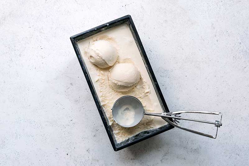 The finished ice cream in the loaf pan with two scoops portioned out and an ice cream scoop.