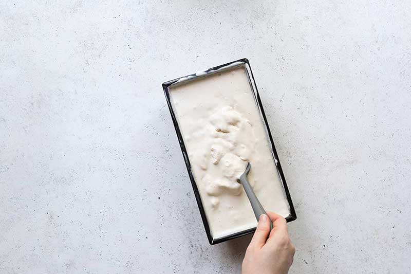 Using a spoon to stir the homemade vanilla ice cream, which is in a 9x5 loaf pan.