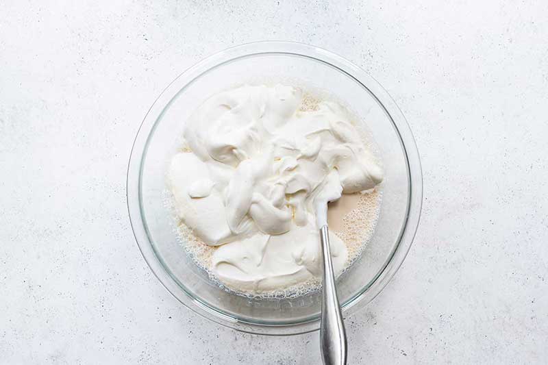 Whipped cream being folded into the other homemade ice cream ingredients with a spatula.