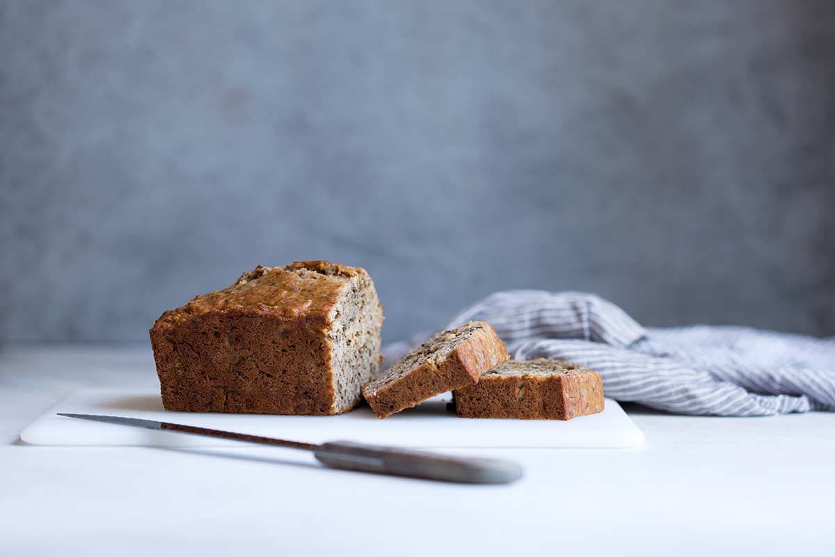 Sliced banana bread on a cutting board next to a serrated knife.