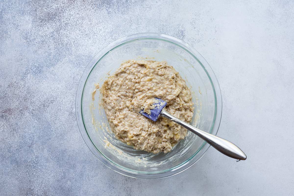 Raw ingredients for banana bread being stirred with a spatula in a pyrex bowl.