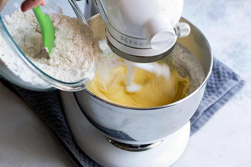 adding dry ingredients to bowl of standing mixer