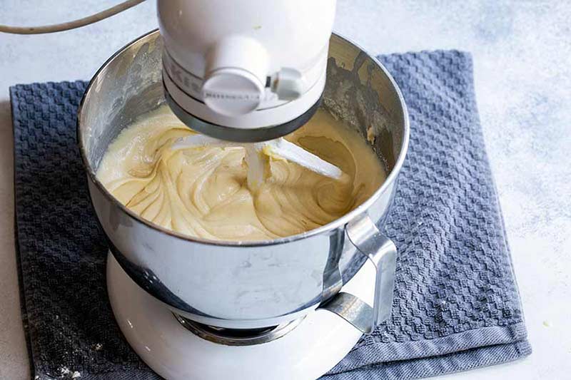 yellow cake batter being whipped in bowl of standing mixer
