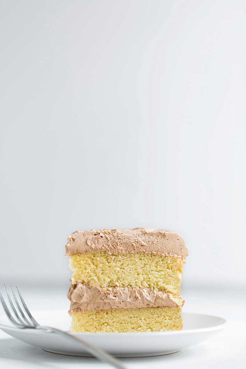 A slice of yellow cake with chocolate frosting