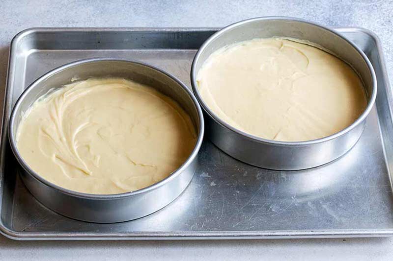 yellow cake batter in two cake pans on metal baking sheet
