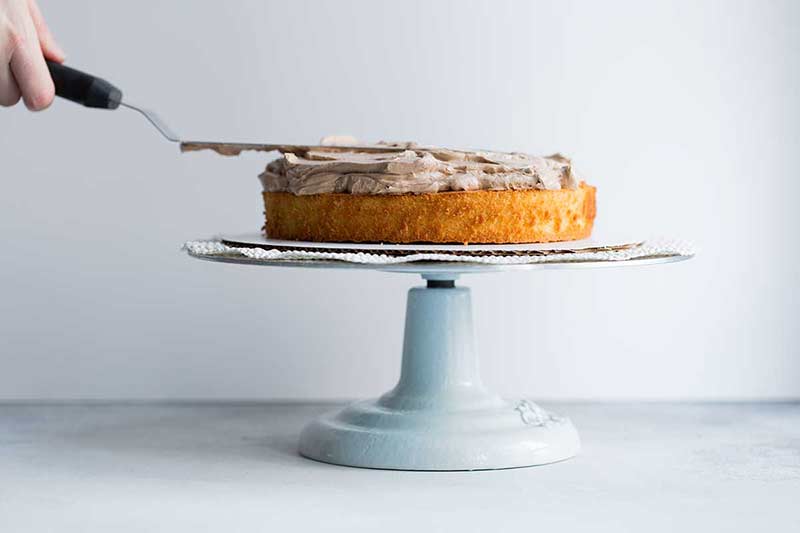 Spreading chocolate frosting onto a layer of yellow cake.