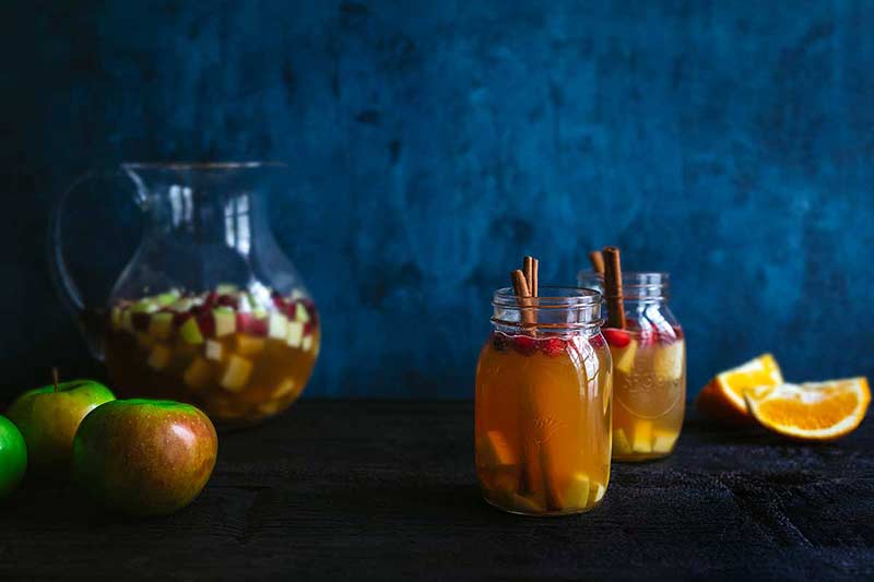 glass pitcher and two mason jar glasses filled with a white wine cocktail made with apples and pears
