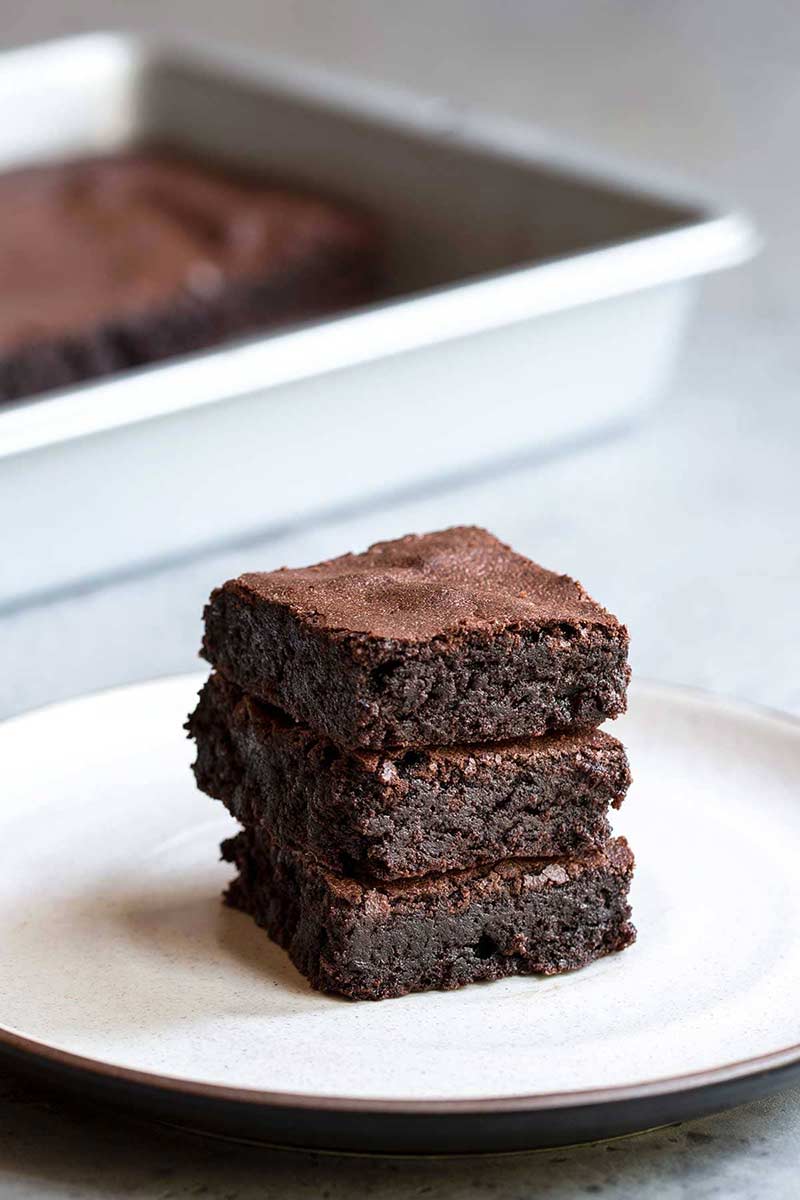 A close up photo of 3 stacked homemade brownies on a plate.