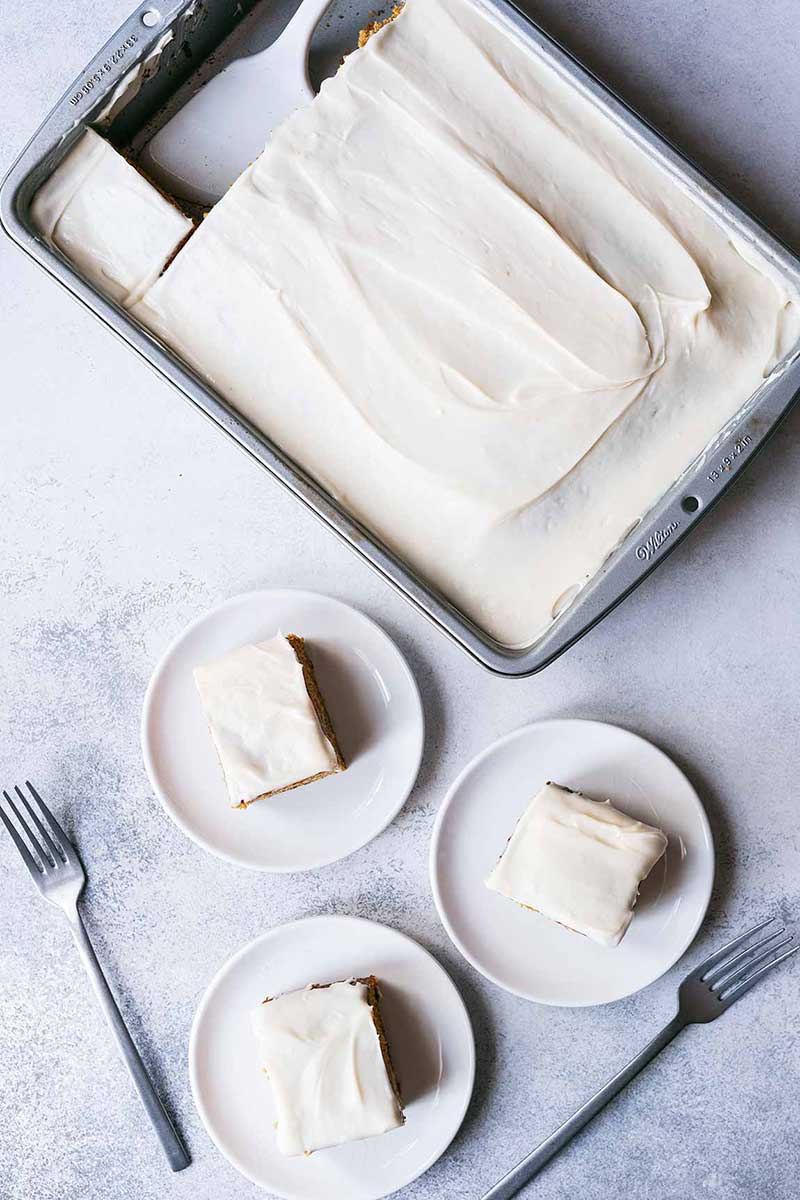 Pumpkin cake with cream cheese frosting in a pan, with three slices on plates.