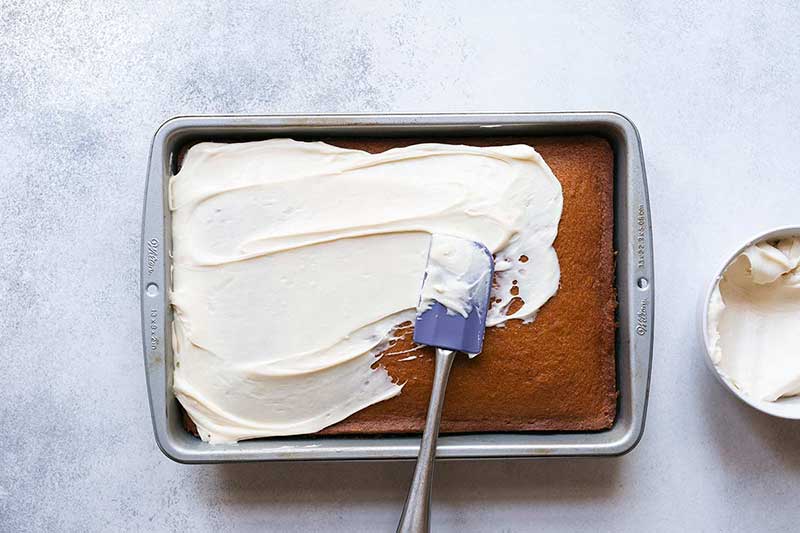 A spatula spreading cream cheese frosting over homemade pumpkin cake