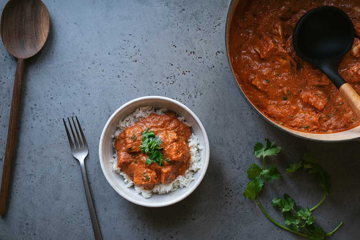 A bowl of chicken tikka masala on a blue backdrop