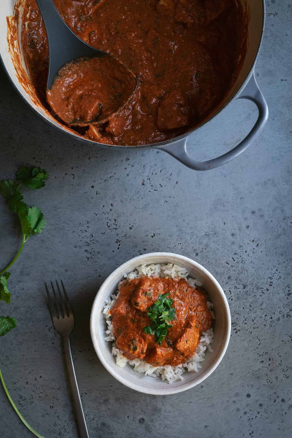 A bowl of chicken tikka masala next to a large pot and ladle