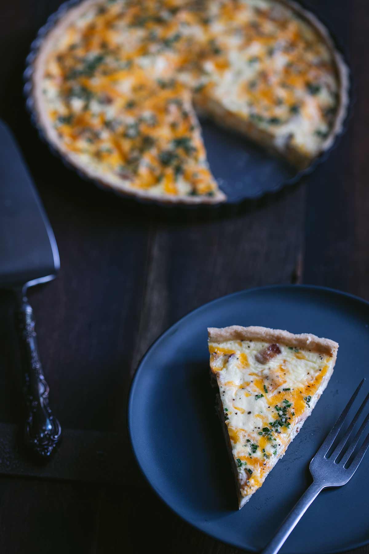 Slice of bacon egg and cheese quiche on a plate.