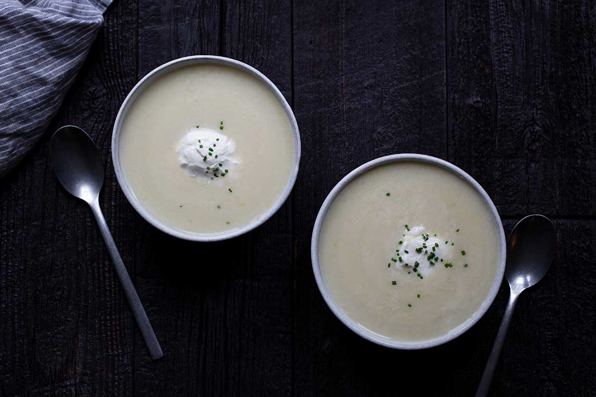 Two bowls of potato leek soup topped with soup cream and chives. Two spoons and a napkin included in photo. 
