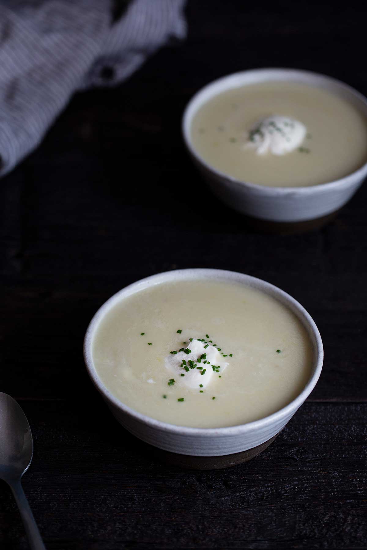 Two bowls of potato leek soup topped with soup cream and chives.