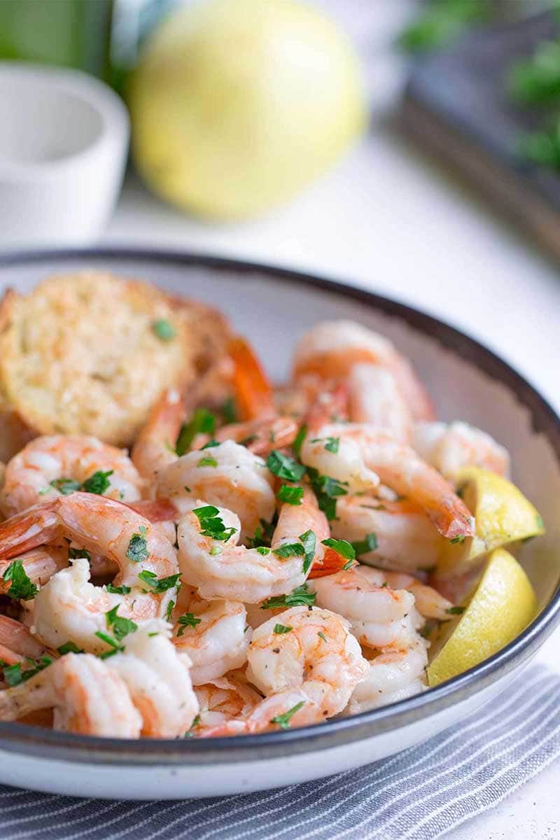 Sheet pan shrimp scampi in a bowl with bread and lemon