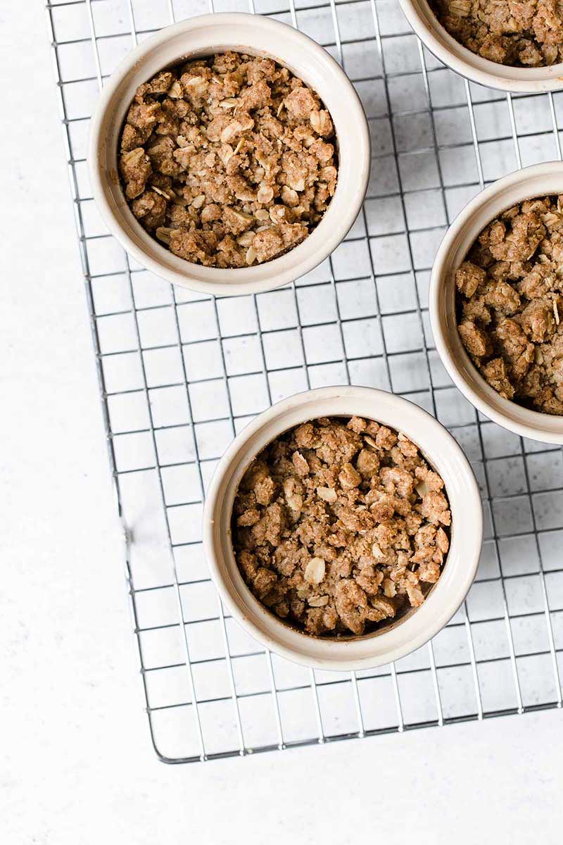 4 apple crumbles in ramekins sitting on a cooling rack