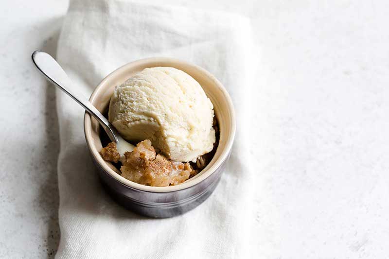 one apple crumble recipe in a ramekin with ice cream and a spoon