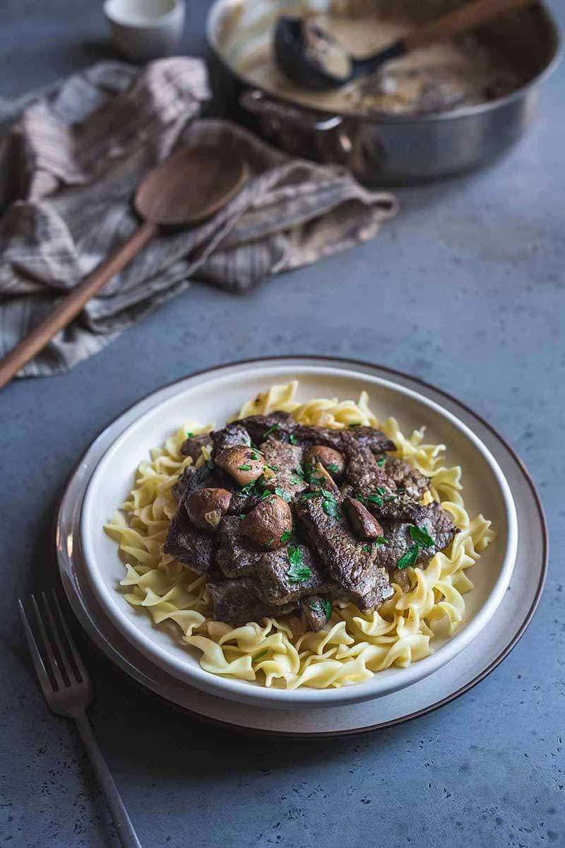 Easy beef stroganoff recipe in a bowl in the foreground, skillet and ladle in the background