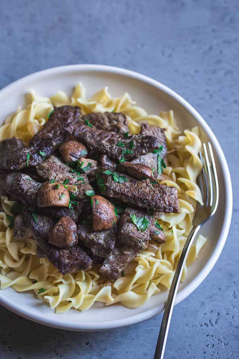 Closeup of beef stroganoff in a bowl, showcasing beed, mushrooms, and fresh parsley