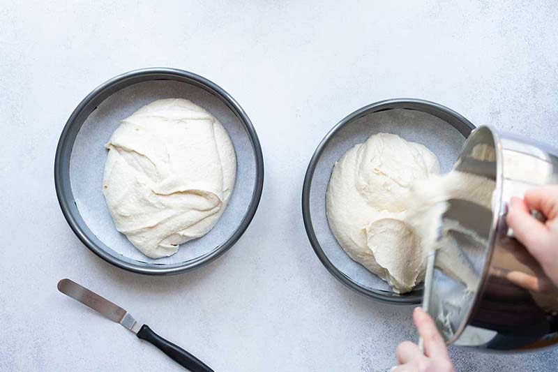 pouring cake batter into two 9-inch cake pans