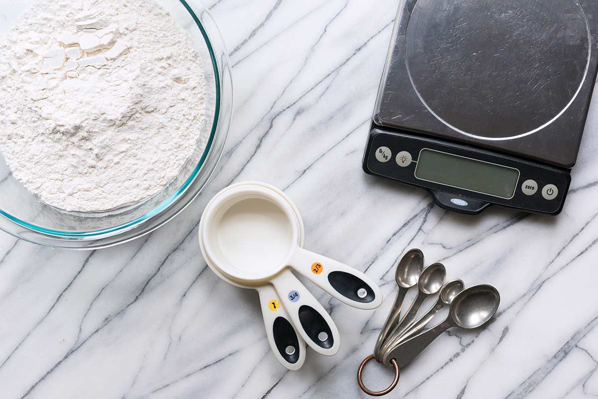 Measuring cups, spoons, a digital scale, and a bowl of flour.